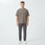 A man modeling a taupe short-sleeve crewneck t-shirt and dark gray trousers against a light gray studio background.