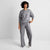 A woman modeling a matching gray knit lounge set consisting of a crewneck sweatshirt and wide-leg pants, photographed against a light gray studio background.