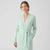 A woman wearing a light mint green knit wrap robe with a tie belt and front patch pockets, photographed against a clean light gray studio background.