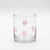 A clear glass tumbler with a circular base decorated with small pink heart shapes outlined in metallic silver, set against a seamless white background.