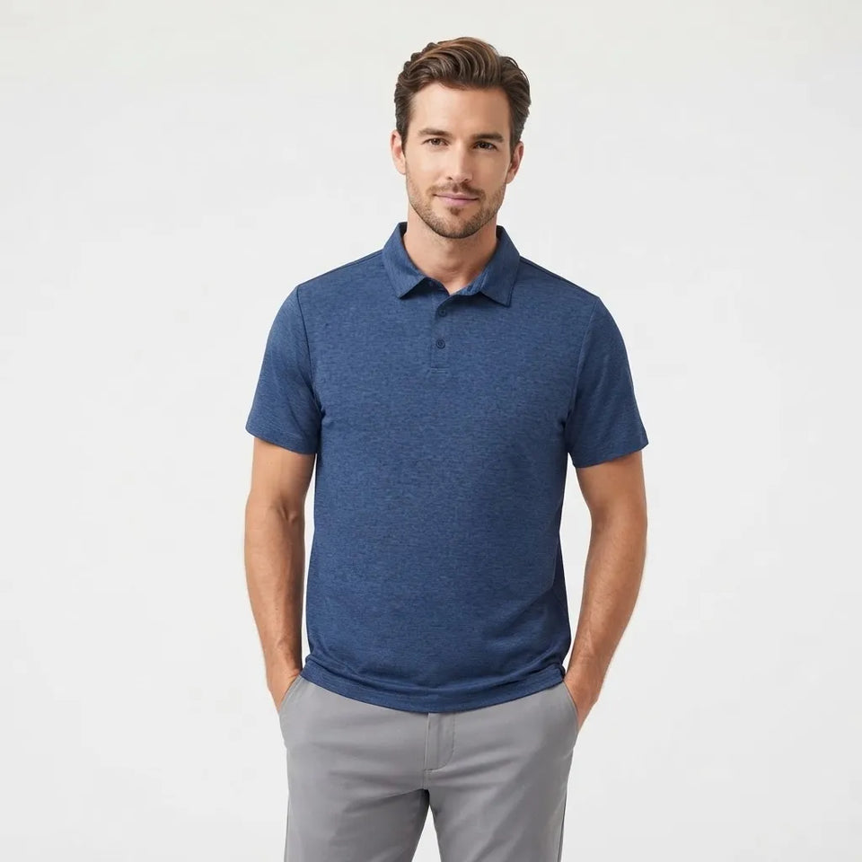 A man wearing a heathered blue short-sleeve polo shirt and light gray trousers, standing against a plain white studio background.