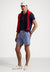 Man wearing a navy polo shirt, blue checkered shorts, red vest, and white cap on a white background