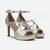 A pair of metallic silver high-heeled sandals with criss-cross ankle straps, cutout details, and a platform sole, shown against a plain light gray background.