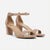 A pair of women's block-heel sandals in a light tan/beige color, featuring double front straps, a low ankle strap with a silver buckle, and square toes, shown against a plain light gray background.