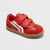 A red toddler sneaker with two hook-and-loop straps, a white side stripe, and a tan rubber sole, shown on a light gray background.