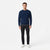 A man modeling a navy blue textured knit crewneck sweater, paired with dark charcoal pants and white sneakers, standing against a plain white studio background.