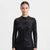 A woman modeling a black long-sleeve top with a sheer mesh mock neck and dense sequin embellishment across the bodice and sleeves, against a plain light gray studio background.