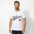 A man wearing a white short-sleeve crewneck t-shirt with a navy blue 'Hilliger' script logo and '85' printed on the front, paired with dark navy pants, set against a plain white studio background.