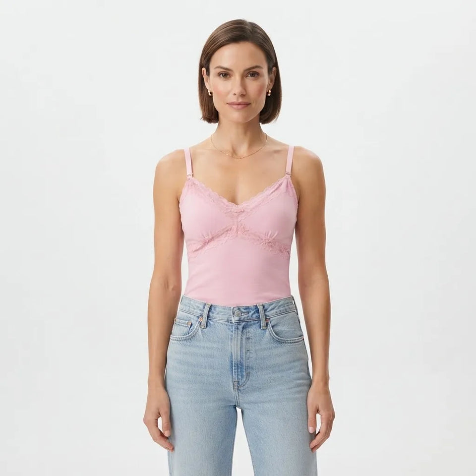 A woman modeling a light pink camisole top with delicate lace trim and ruffle details, paired with light-wash blue jeans, against a plain white studio background.