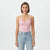 A woman modeling a light pink camisole top with delicate lace trim and ruffle details, paired with light-wash blue jeans, against a plain white studio background.