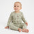 A baby sitting on a white studio background wearing a sage green long-sleeve pajama set with a brown animal print.