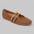 A tan perforated leather flat shoe with two decorative straps and gold-tone buckle details, shown on a neutral gray background.