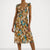 A woman modeling a sleeveless midi wrap dress with a floral print in beige, brown, and turquoise blue, paired with matching blue high-heeled sandals against a light gray studio background.