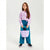 A young girl stands against a light gray studio background wearing a lavender fuzzy sweater with white cloud patterns, teal wide-leg pants, black boots, and holding a lavender quilted puffer handbag.