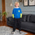 A young boy stands in a living room wearing a bright blue sweatshirt with neon green sleeves, black cargo pants, and white sneakers. The sweatshirt features a white hood and a yellow graphic logo on the left chest.