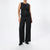A model wearing a black sleeveless textured vest with a peplum waist and a single gold button, paired with black wide-leg trousers and black shoes, against a plain white studio background.