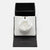 A white fabric flower brooch displayed on a white textured insert inside an open black presentation box. The brand name Hookandalbert.