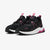 A pair of Puma sneakers in black and white with vibrant pink accents, including the Puma logo, heel detail, and pull tabs, shown on a light gray background.