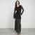 A woman modeling a black long-sleeve lace maxi dress with a fitted bodice and sheer lace skirt, standing against a light gray studio background.