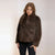 A woman modeling a dark brown faux fur jacket with a wide collar, paired with black pants, against a plain light background.