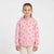 A young girl with her hair pulled back stands against a light gray studio background wearing a pink zip-up hoodie with a small black bow pattern and white pants.