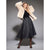 A woman modeling a light beige faux fur jacket over a black top and a black pleated tulle midi skirt, standing against a gray studio background.
