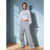 A woman modeling a light gray cropped sweatshirt and matching wide-leg sweatpants in a studio setting with a blue wall and wooden floor.