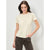 A woman modeling a short-sleeve crewneck t-shirt in a light cream color, paired with dark brown pants, against a light gray studio background.