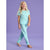 A young girl with long blonde hair stands barefoot against a solid lavender studio background, wearing a light mint green two-piece pajama set with a small rainbow graphic on the chest.