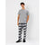 A man modeling a light gray crewneck t-shirt and black-and-white plaid pajama pants with black slip-on socks, standing against a light gray studio background.
