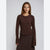 A woman modeling a dark brown ribbed knit long-sleeve top with a flared bell sleeves and a ruffled hem, paired with a matching brown textured skirt, against a plain light gray background.