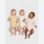 Three babies lying side by side on a light gray studio background, wearing long-sleeve bodysuits in pale yellow with tiny dark dots, cream, and light pink. The babies are smiling and laughing.