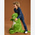 A smiling child wearing navy blue pajamas with a white space-themed print is hugging a large green plush dinosaur toy against a solid brown studio background.