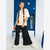 A girl with long braided hair stands in a school locker room setting, wearing a cream-colored oversized t-shirt, black wide-leg pants, and white sneakers.