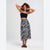 A woman modeling a black and white zebra-print midi skirt with a black spaghetti-strap crop top, standing against a light gray studio background.