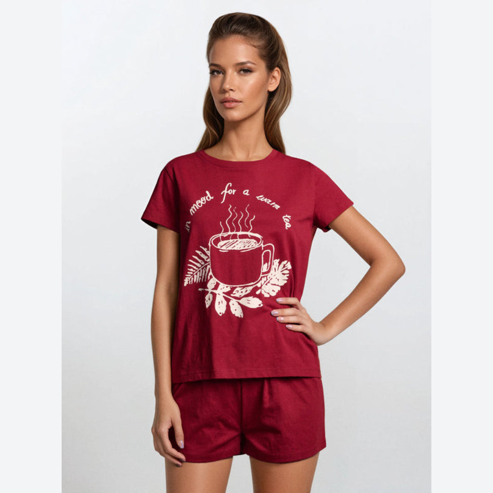 A woman modeling a matching two-piece pajama set consisting of a short-sleeve t-shirt and shorts in deep red. The t-shirt features a white graphic print of a steaming coffee cup with leaves and the text 'enjoy for a warm day'.