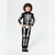 A child wearing a black and white skeleton-themed long-sleeve pajama set with matching socks, standing against a light gray studio background.