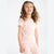 A young girl with curly brown hair wearing a light pink ribbed two-piece pajama set with a small floral print, standing against a plain white background.
