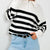 A person wearing a black and white horizontally striped half-zip knit sweater with a white collar, paired with light blue jeans and a black belt.