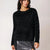 A woman wearing a black fuzzy long-sleeve crewneck sweater and a silver sequined skirt, photographed against a plain light background.
