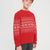 A young boy wearing a red knit sweater with a white Nordic pattern, paired with dark gray pants, photographed against a light gray studio background.