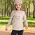 A young girl wearing a beige knit sweater with a pink sequined hedgehog graphic, a matching beige cat-ear beanie, and dark ribbed pants, standing in a blurred park setting.