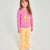 A young girl with long light brown hair stands against a plain light gray studio background, wearing a bright pink long-sleeve sweatshirt with a yellow leopard-print graphic on the front, paired with mustard yellow pants and white sneakers.
