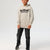 A child wearing a light heather gray hoodie with a black 'noise!' graphic on the chest, paired with dark gray pants and black sneakers, standing against a light gray studio background.