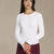 A woman wearing a white ribbed long-sleeve crewneck sweater and burgundy trousers, standing against a solid beige studio background.