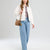 A model wearing a white cropped jacket, a red and white striped t-shirt, light blue wide-leg jeans, and carrying a brown leather shoulder bag with a yellow tassel charm, set against a light gray studio background.