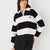 A woman wearing a black and white horizontally striped long-sleeve rugby-style top with a small embroidered cherry motif on the left chest, paired with black pants against a plain light background.