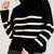 A close-up of a person wearing a black ribbed knit sweater with horizontal white stripes across the chest and sleeves, paired with gray bottoms against a light gray background.
