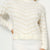 A close-up of a person wearing a cream knit sweater with thin beige chevron stripes and a ribbed turtleneck and cuffs, paired with a matching ribbed skirt against a plain light background.