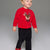 A toddler wearing a bright red fuzzy knit sweater with a sequined reindeer face on the front, paired with black pants featuring small white polka dots, standing against a neutral gray studio background.